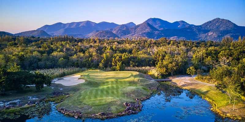 Parcours de golf entouré d’eau devant des montagnes en Thaïlande