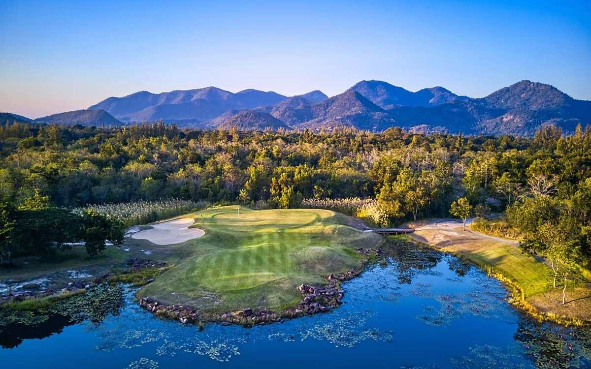 Parcours de golf entouré d’eau devant des montagnes en Thaïlande